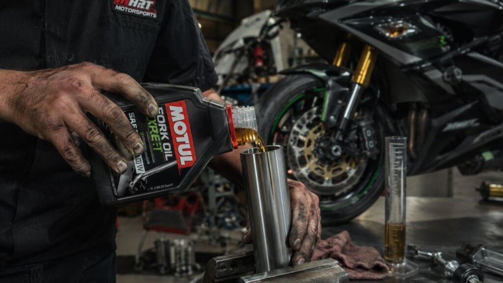Mechanic pouring best fork oil into motorcycle front fork leg in workshop