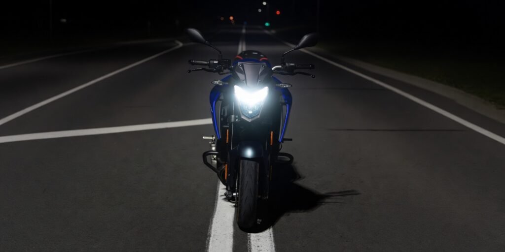 Motorcycle on a dark road at night with a bright LED headlight beam illuminating the road ahead