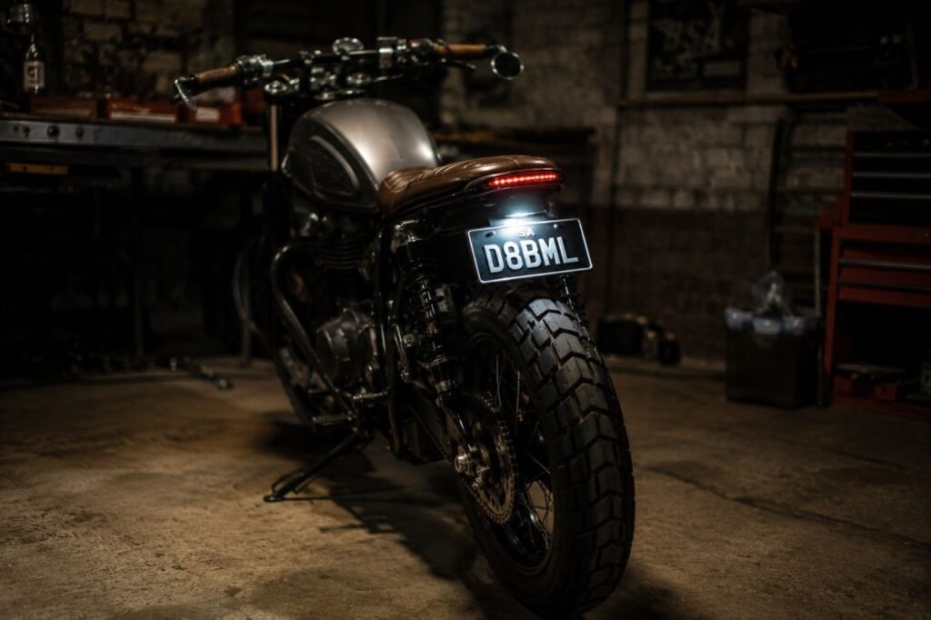 Integrated motorcycle tail light kit glowing red on custom scrambler rear end in garage