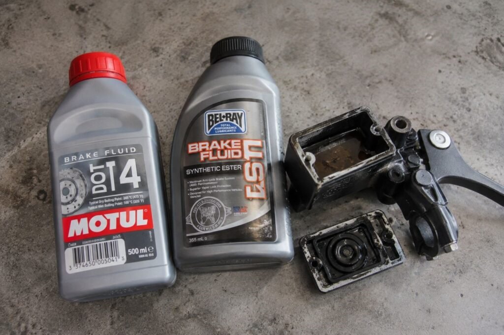 DOT 4 and DOT 5.1 brake fluid bottles next to a motorcycle master cylinder reservoir