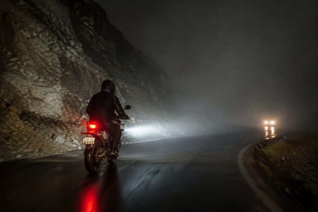 Motorcycle riding at night on wet mountain road showing need for LED lighting upgrade