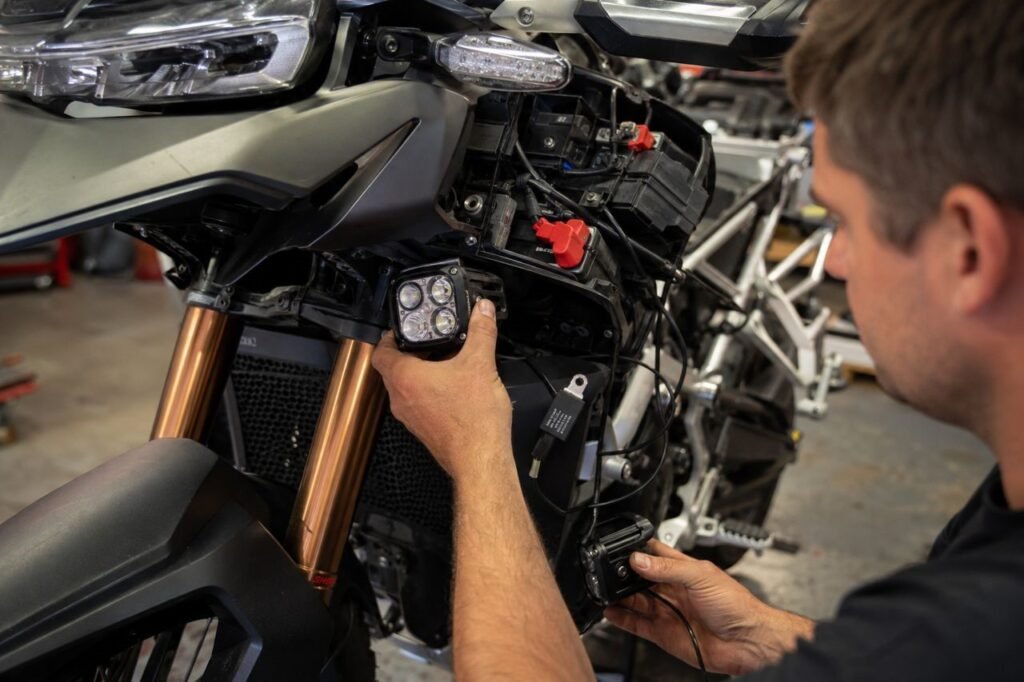 Motorcycle mechanic installing LED auxiliary lights with relay wiring in workshop