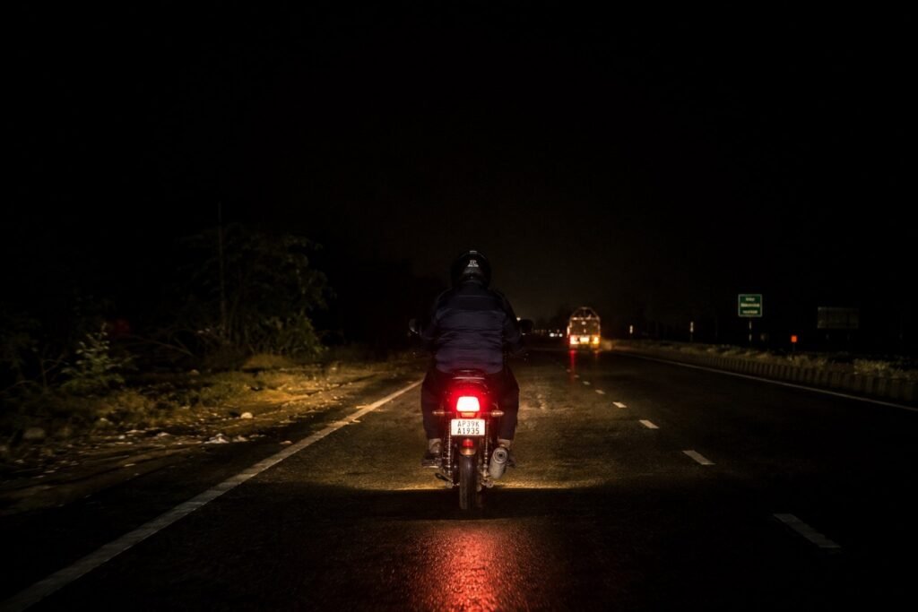 Motorcycle rider on a dark highway at night with a dim stock headlight
