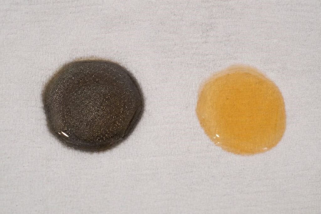 Two fork oil samples on white paper showing color difference between synthetic and mineral motorcycle fork oil
