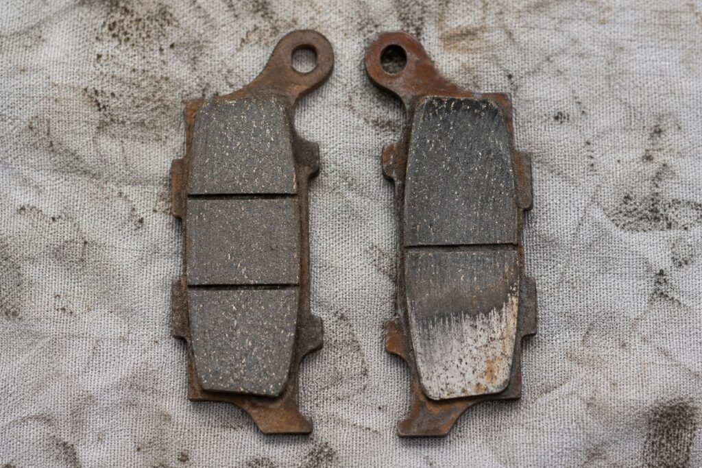 Two used motorcycle brake pads side by side showing even wear versus taper wear caused by a seized caliper slide pin