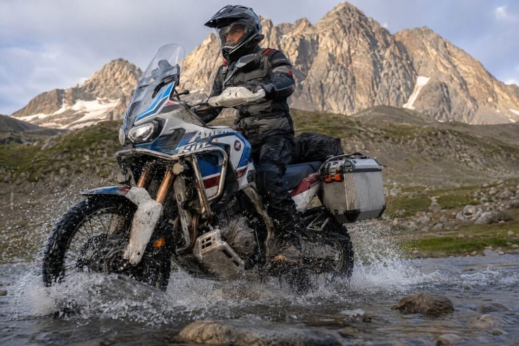 Adventure motorcycle crossing rocky river showing need for wet chain lube