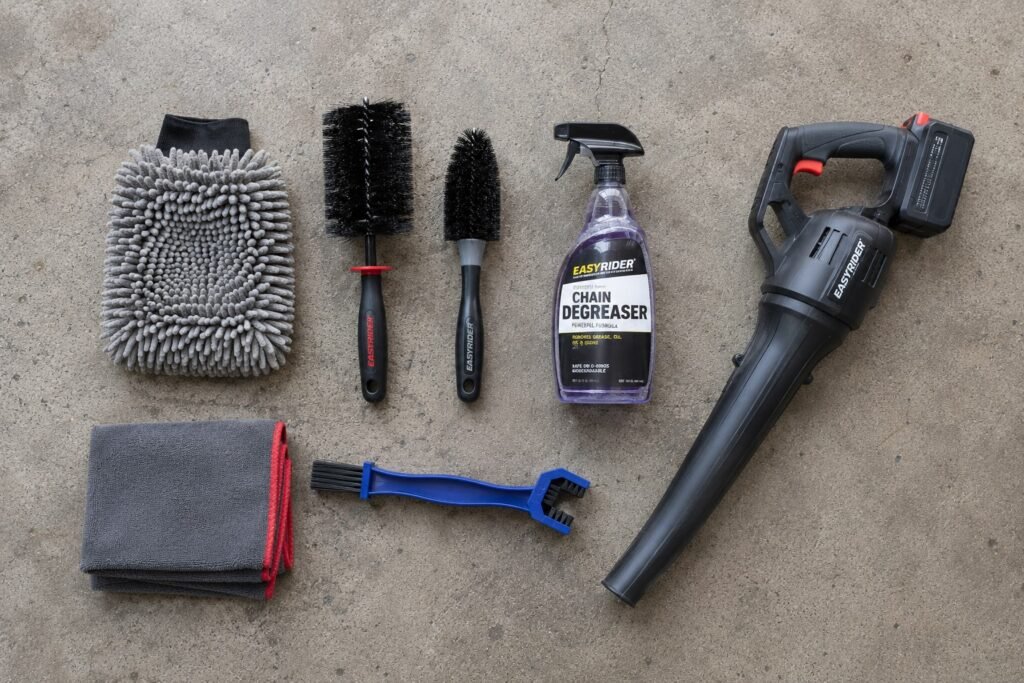 Complete motorcycle cleaning kit laid out on garage floor including wash mitt, wheel brushes, chain degreaser, and microfiber towels.
