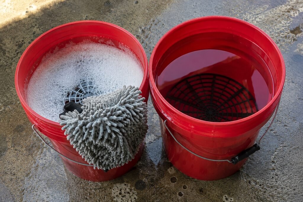 Two buckets with grit guards set up for the two-bucket motorcycle washing method on a garage floor.