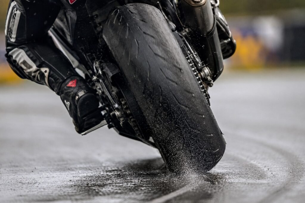Close-up of a motorcycle tire contact patch leaning into a corner on wet asphalt