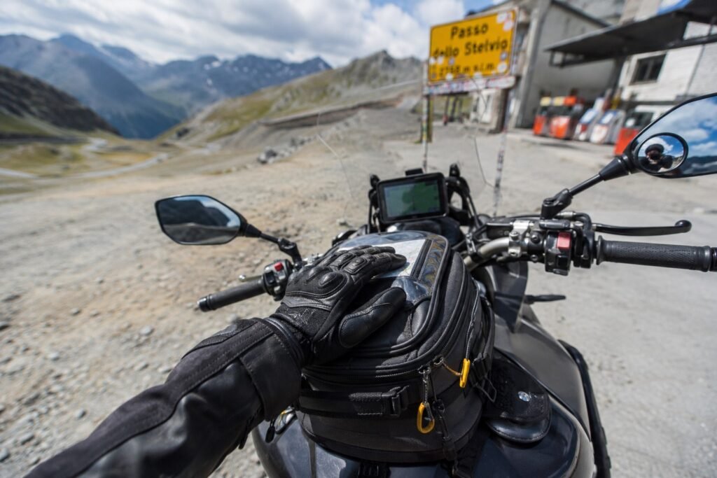 Rider's hand resting on a motorcycle tank bag mounted on a fuel tank during a touring stop